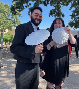 Karen Salkin with her new bestie, Rod Bastanmehr, before the actual wedding began, modeling the thoughtful little paper parasols that were given out because some of us sat in the sun there. Photo by Harry Calianes.